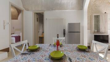 A dining area with a table set for two, a refrigerator, and a kitchen area with a microwave.