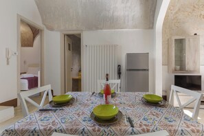 A dining area with a table set for two, a refrigerator, and a kitchen area with a microwave. - AquaTerrae by BarbarHouse (Alezio)