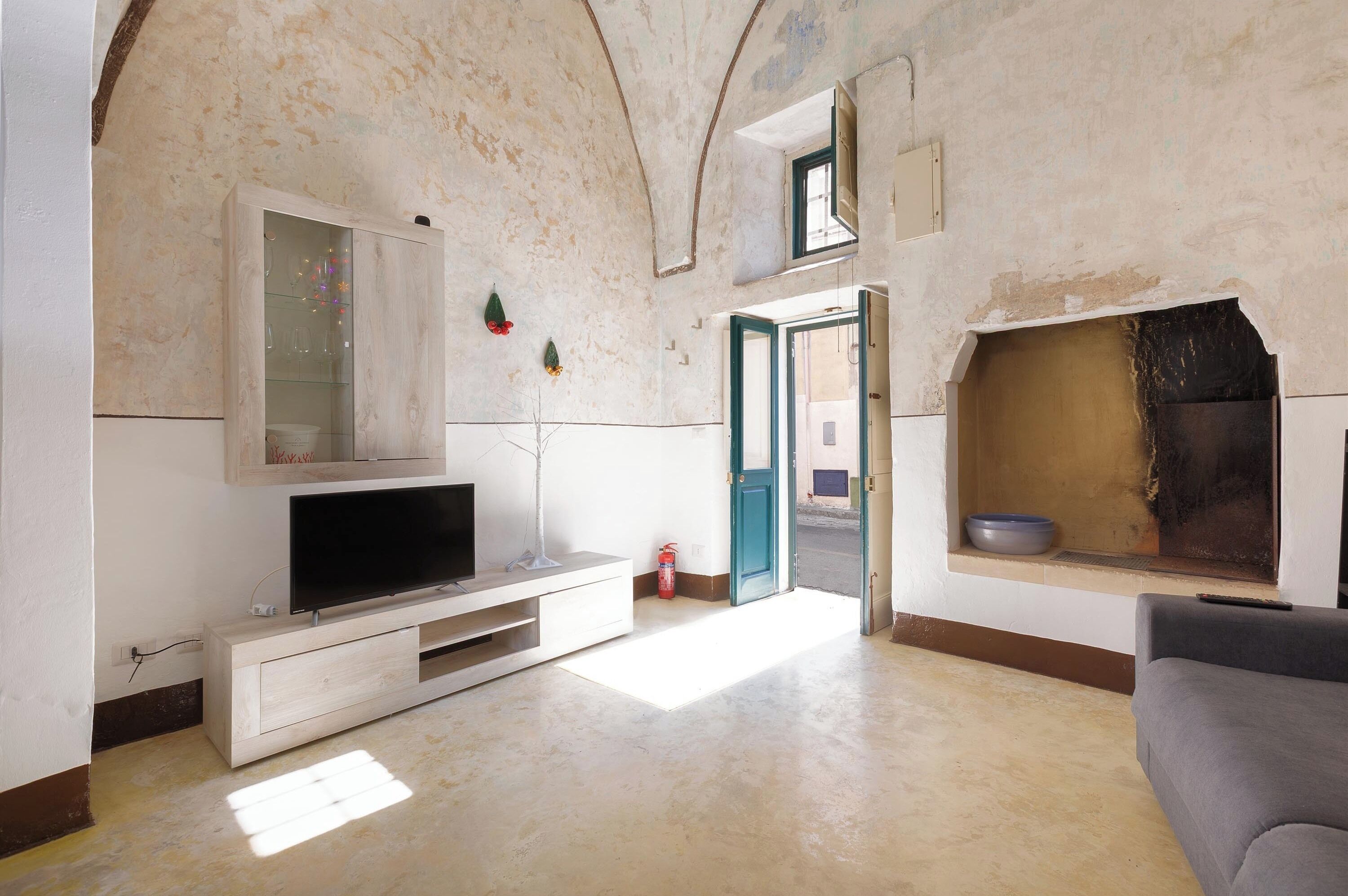 A living room with a television on a wooden stand, a fireplace, and a door leading outside.