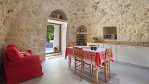A stone-walled room with a dining area, a red sofa, and a kitchen with a microwave. - Pajara Donna Piccinni by BarbarHouse (Carpignano Salentino)