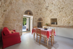 A stone-walled room with a dining area, a red sofa, and a kitchen with a microwave. - Pajara Donna Piccinni by BarbarHouse (Carpignano Salentino)