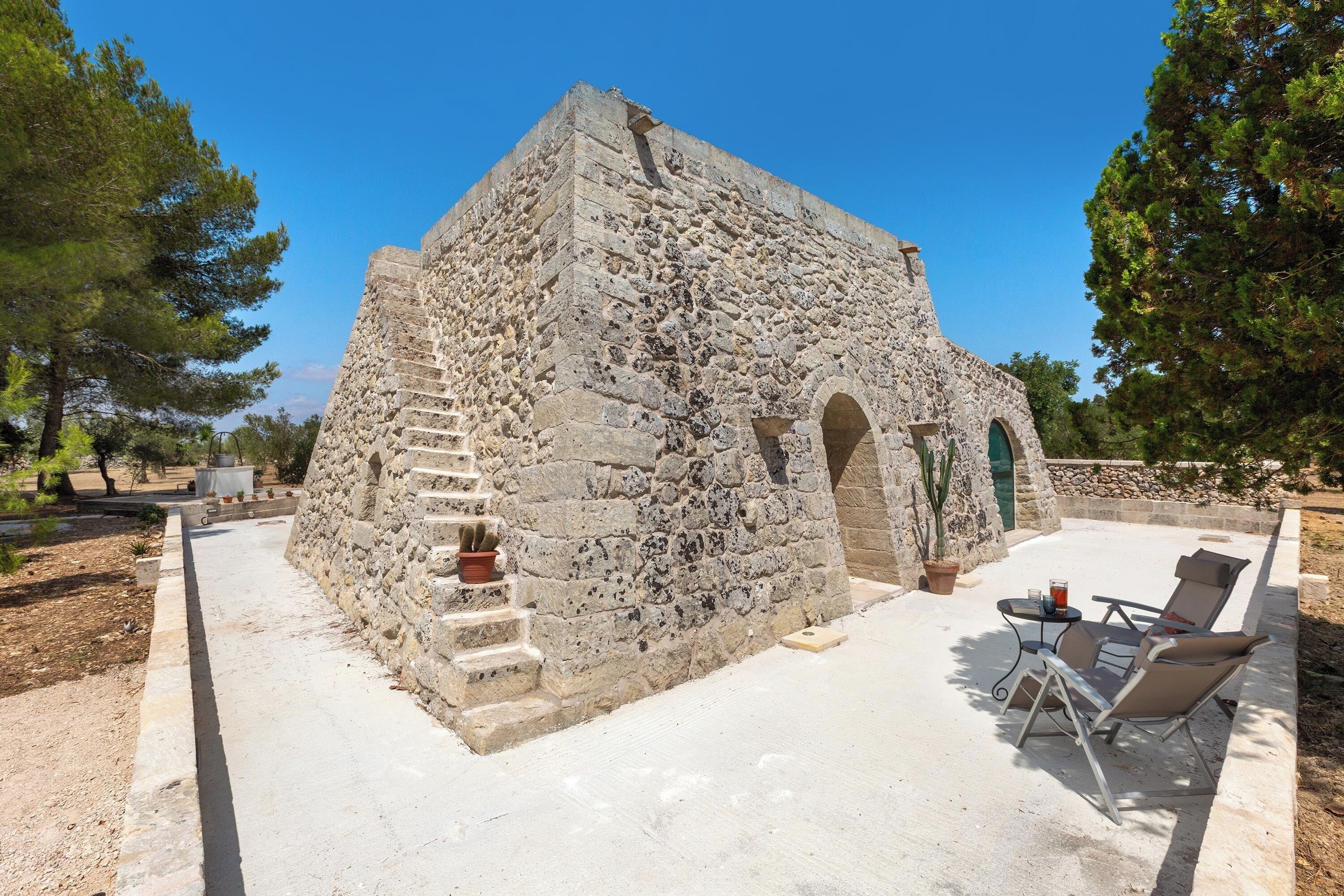 Un bâtiment en pierre avec un escalier, une porte et une petite table entourée de chaises.