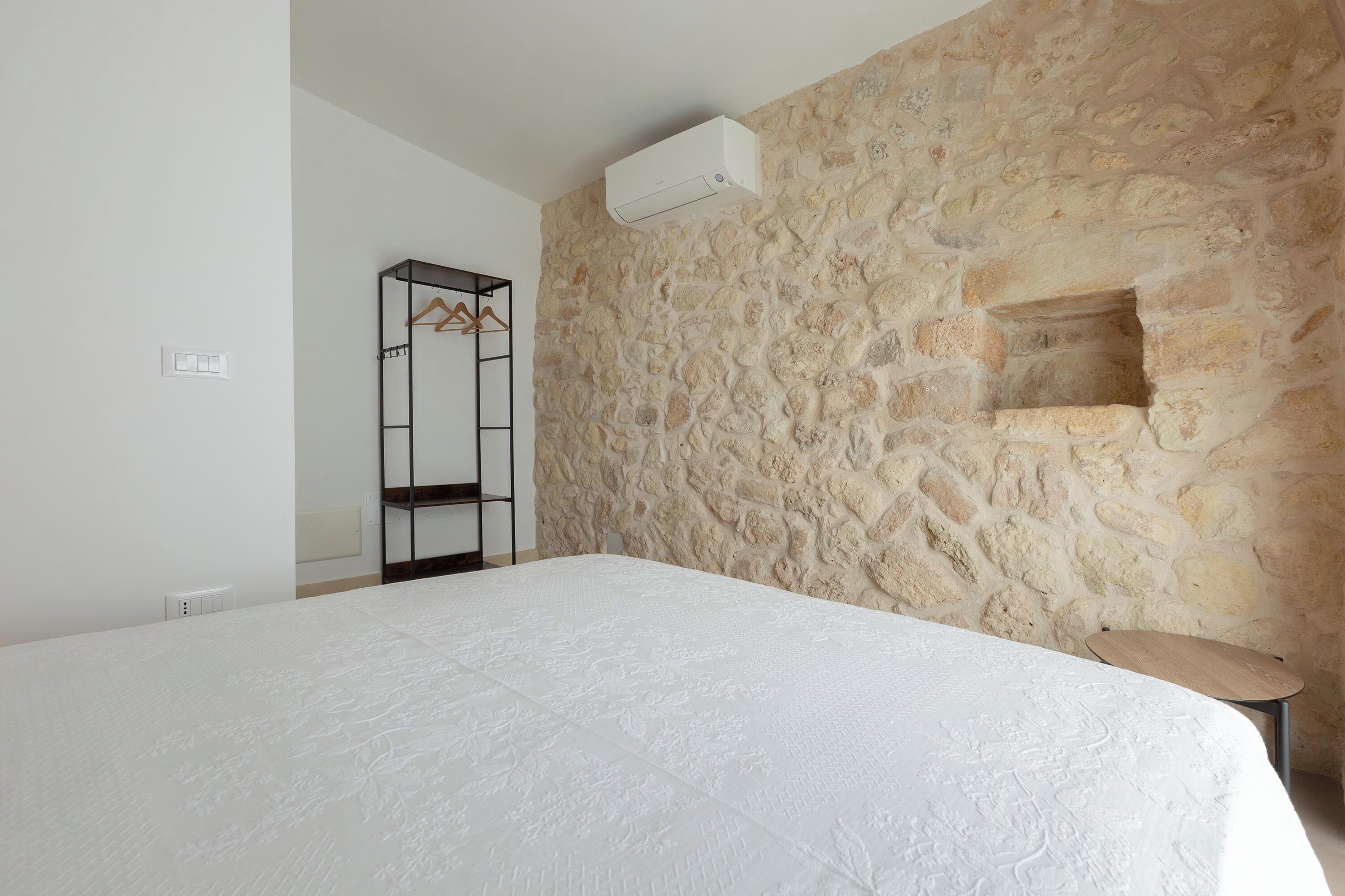 A bedroom with a large bed, a wardrobe, a small window, and a stone wall.