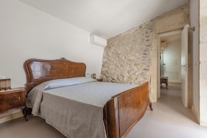 A bedroom with a wooden bed, a stone wall, and a door leading to another room. - Pajara Donna Piccinni by BarbarHouse (Carpignano Salentino)