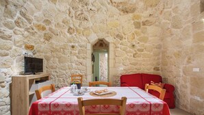 A stone-walled room with a dining table set for two, a television, and a red sofa. - Pajara Donna Piccinni by BarbarHouse (Carpignano Salentino)