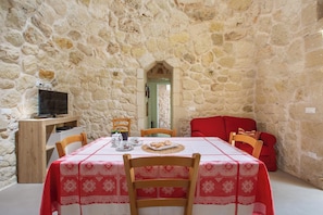 A stone-walled room with a dining table set for two, a television, and a red sofa. - Pajara Donna Piccinni by BarbarHouse (Carpignano Salentino)