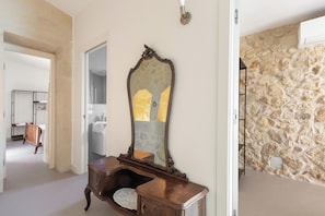 A room with a stone wall, a wooden dresser with a mirror, and a door leading to another room. - Pajara Donna Piccinni by BarbarHouse (Carpignano Salentino)