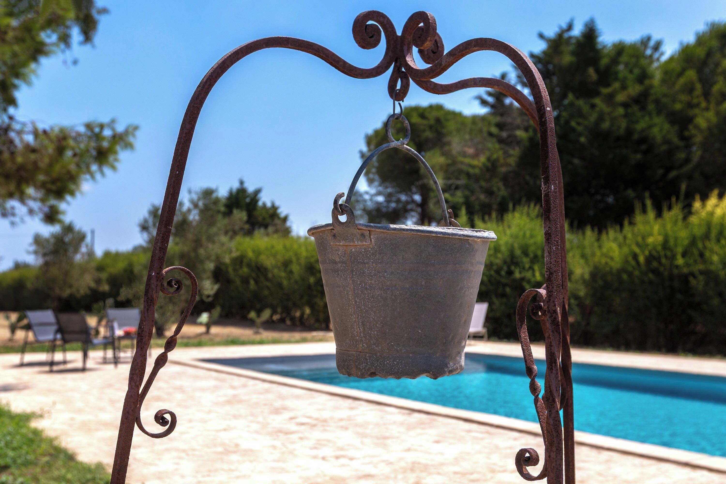 A metal bucket suspended by a decorative metal frame over a pool.