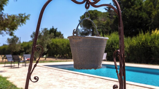 A metal bucket suspended by a decorative metal frame over a pool. - Pajara Donna Piccinni by BarbarHouse (Carpignano Salentino)