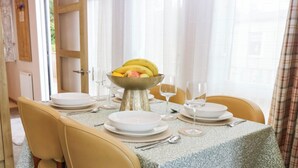 Une table à manger dressée avec de l’argenterie, des assiettes blanches et un saladier rempli de fruits.