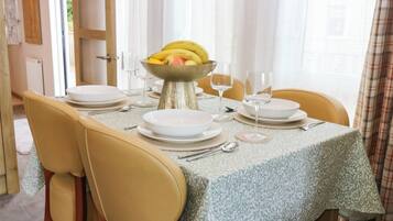 A dining table set with white plates, silverware, and a fruit bowl.
