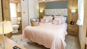 Une chambre à coucher avec un lit, des tables de chevet, une lampe, un luminaire fixé au mur et une fenêtre avec des rideaux.