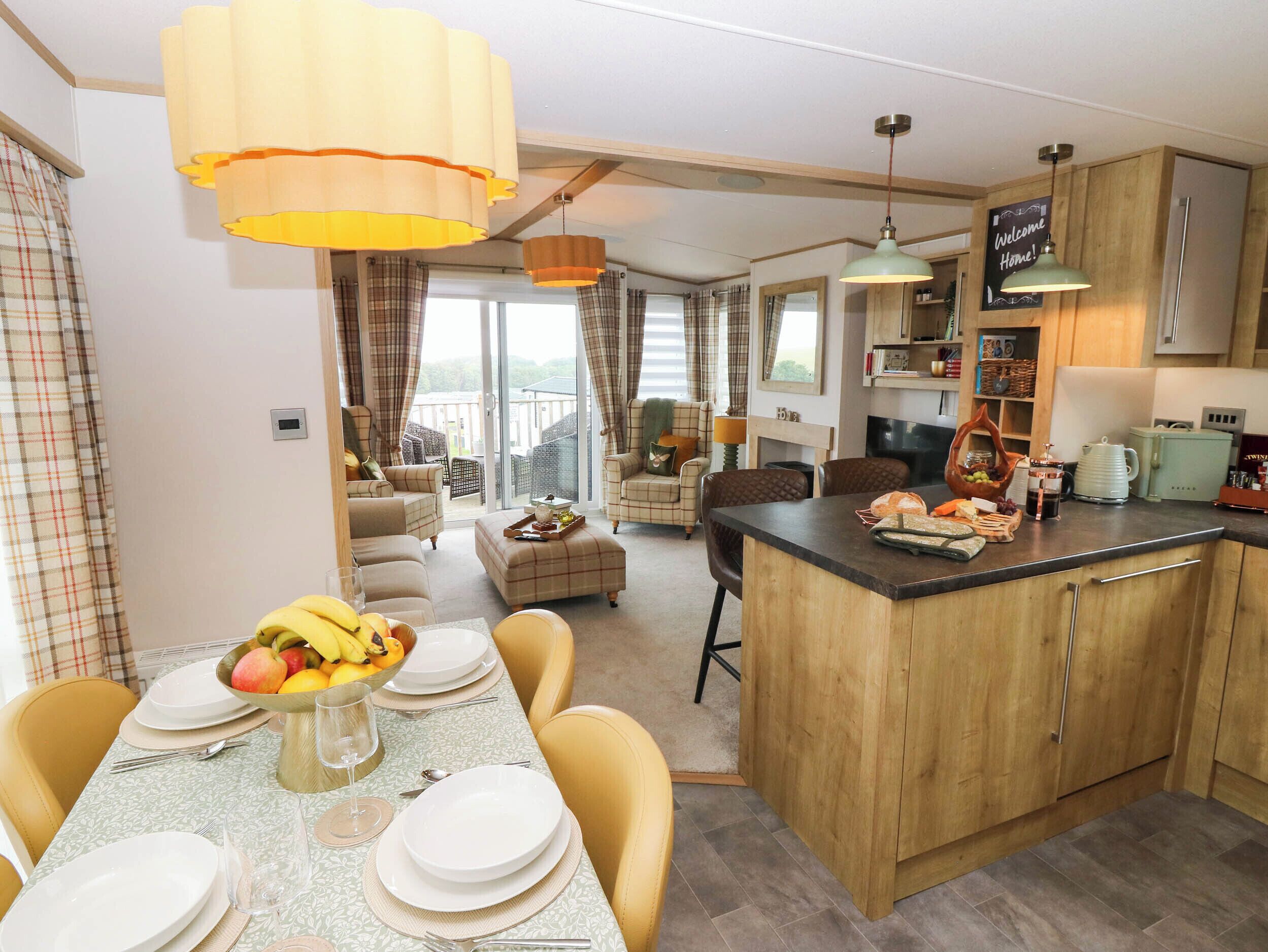 A modern kitchen with a central island, dining area with a table set for four, and a living area with a sofa and chairs.