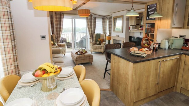 Une cuisine moderne dotée d’un îlot central, d’un coin repas avec une table pour quatre personnes et d’un salon avec un canapé et des fauteuils.