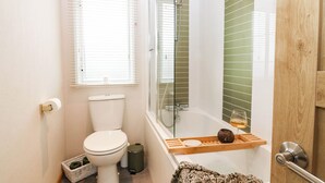 Une petite salle de bain comprenant des toilettes, un espace douche et une fenêtre avec des stores.