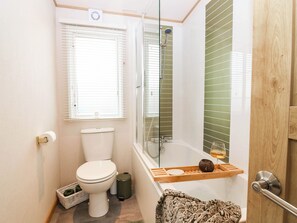 A compact bathroom with a toilet, a shower enclosure, and a window with blinds. - The Manors Retreat (Dunbar)