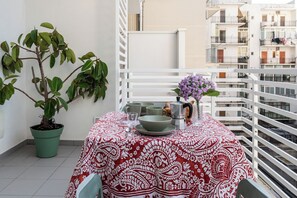 Ein Balkon mit Tisch für zwei Personen, einem Blumentopf und Blick auf die umliegenden Gebäude.