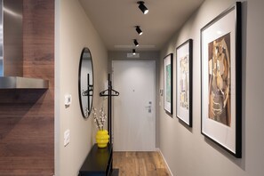 A hallway with a wooden floor, a mirror, a black bench, a yellow vase with branches, and framed artwork on the walls. - Gallo Studio  by BarbarHouse (Bari)