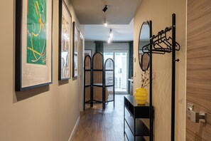 A hallway with framed artwork on the walls, a black metal rack with hooks, and a yellow vase on a black shelf. - Gallo Studio  by BarbarHouse (Bari)