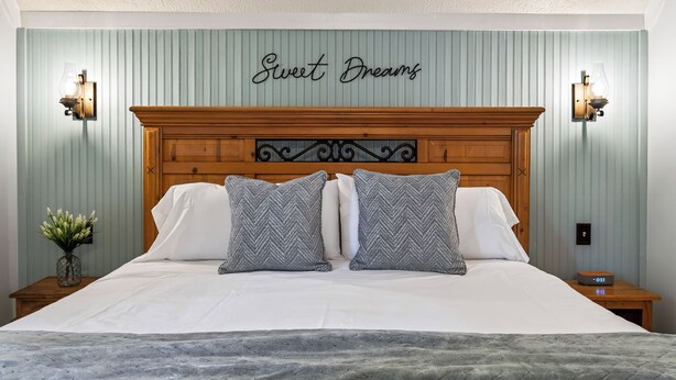Ein Schlafzimmer mit einem Bett, zwei Nachttischen, Wandleuchten, einem dekorativen Schild und einer Uhr.