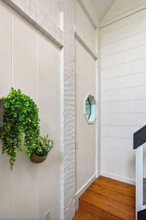 A hallway with white walls, a wooden floor, a hanging plant, and a wall-mounted mirror. - New! Hot Tub/Game Room-Close to Dollywood (Pigeon Forge)