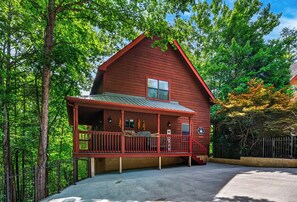 A red wooden cabin with a porch, surrounded by trees. - New! Hot Tub/Game Room-Close to Dollywood (Pigeon Forge)