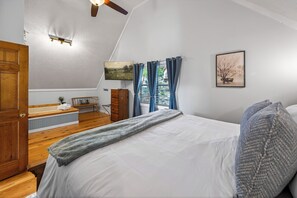 Ein Schlafzimmer mit einem Bett, einer Holzkommode, einem Fernseher und einem Fenster mit Vorhängen.