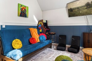 A room with a blue sofa, colorful pillows, a wooden cabinet, and a gaming chair. - New! Hot Tub/Game Room-Close to Dollywood (Pigeon Forge)