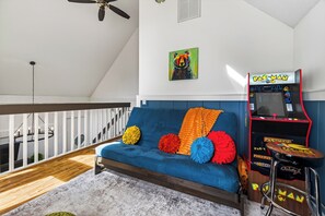 A room with a blue sofa, colorful pillows, a Pac-Man arcade machine, and a ceiling fan. - New! Hot Tub/Game Room-Close to Dollywood (Pigeon Forge)