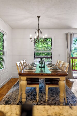A dining room with a wooden table, chairs, a chandelier, and a view of greenery through the window blinds. - New! Hot Tub/Game Room-Close to Dollywood (Pigeon Forge)