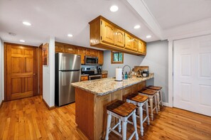 Une cuisine dotée de meubles en bois, d’appareils électroménagers en acier inoxydable, d’un comptoir en granit et de tabourets de bar.