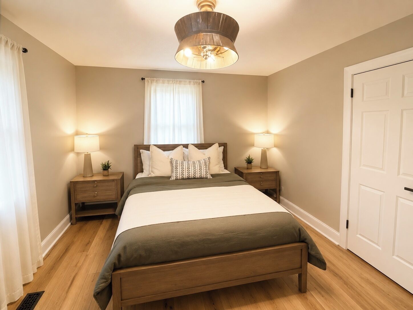 Una camera da letto con un letto, due comodini, un tavolino, una finestra con tende, una porta e una lampada a soffitto.