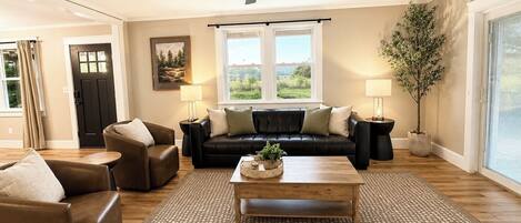 A living room with a black leather sofa, two side chairs, a wooden coffee table, and a ceiling fan.