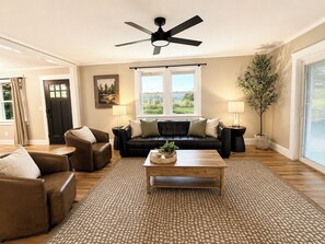 Un salon avec un canapé en cuir noir, deux fauteuils, une table basse en bois et un ventilateur de plafond.