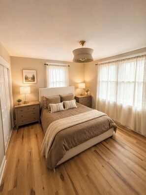 A bedroom with a bed, nightstands, a lamp, a picture on the wall, and a window with curtains.