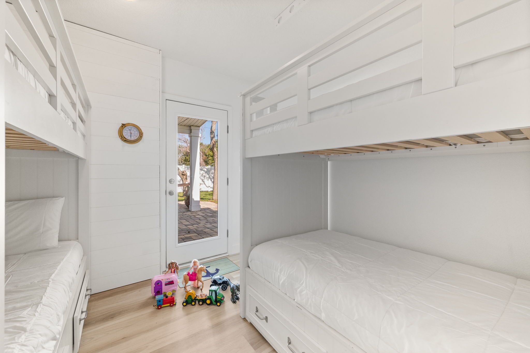 A child's bedroom with bunk beds, a door leading outside, and toys on the floor.