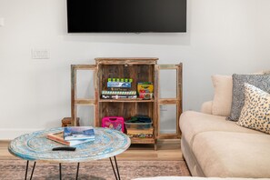 Ein Wohnzimmer mit einem Holzkabinett, einem runden Couchtisch mit Büchern, einer Couch und einem an der Wand befestigten Fernseher.
