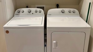 A laundry room with two white Whirlpool washers and dryers, white cabinets above, and a wooden floor.