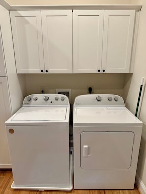 Un lavadero con dos lavadoras y secadoras Whirlpool blancas, armarios superiores blancos y suelo de madera.