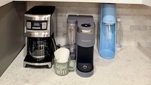 A kitchen with a coffee maker, a kettle, and various mugs on shelves.