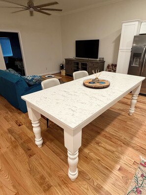 A dining area with a marble table, white chairs, a television, and a refrigerator.