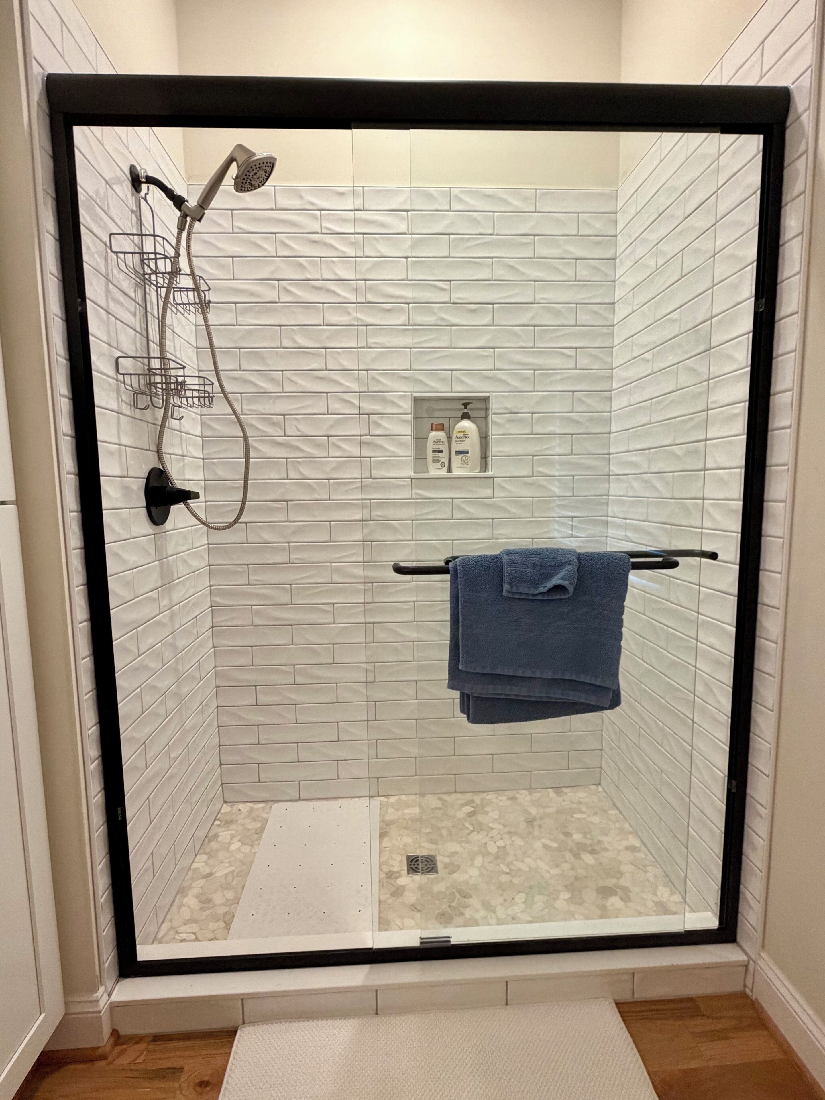Une douche fermée par des parois en verre, avec un porte-serviettes et des articles de toilette.
