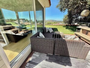 A modern outdoor living space with a wicker sofa, a small round table, and a view of a green landscape. - Spanish Colonial Hilltop Retreat with 360° Views and Rooftop Deck (Los Angeles)