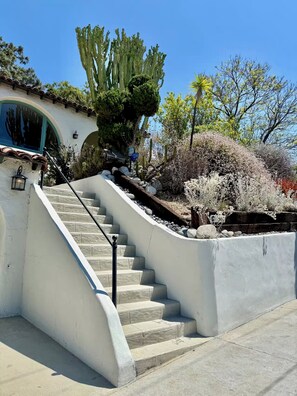 A concrete staircase leading up to a building with a white facade, surrounded by various plants and a cactus. - Spanish Colonial Hilltop Retreat with 360° Views and Rooftop Deck (Los Angeles)