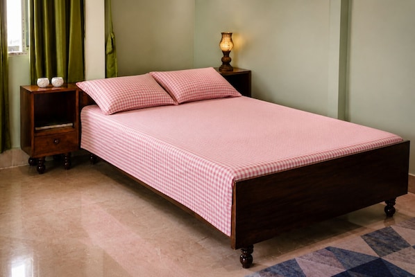A bed with a checkered bedspread, two pillows, a nightstand with a lamp, and a small drawer.
