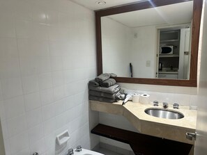 A bathroom with a sink, mirror, towel stack, toilet paper, and a shower area. - Apartment 7/707 (Buenos Aires)
