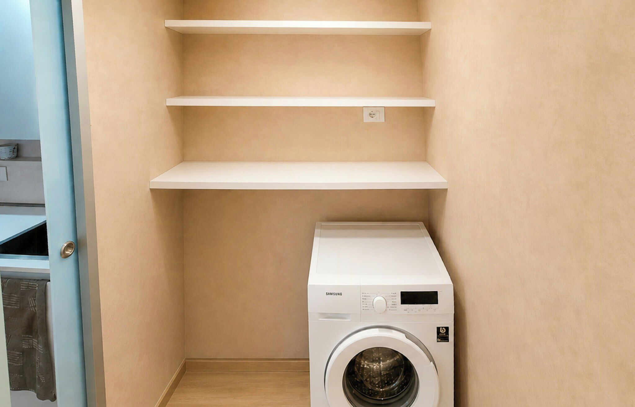 Une buanderie avec un lave-linge blanc et trois étagères vides.