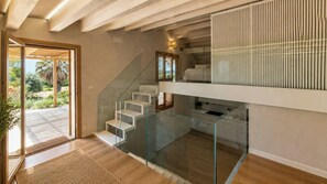 Ein modernes Interieur mit einer Glasstiege, die zu einem Balkon und einer Küchenzeile führt, mit Blick auf einen Garten.