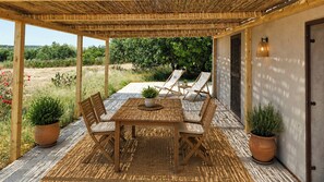 Een terras buiten met een houten tafel en stoelen, omringd door potplanten en een pergola.