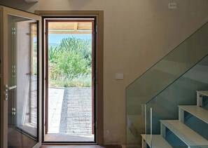 A modern interior with a glass door leading to an outdoor area, a staircase with glass railings, and a plain wall. - Restored cottage with views over Vendicari (Noto)